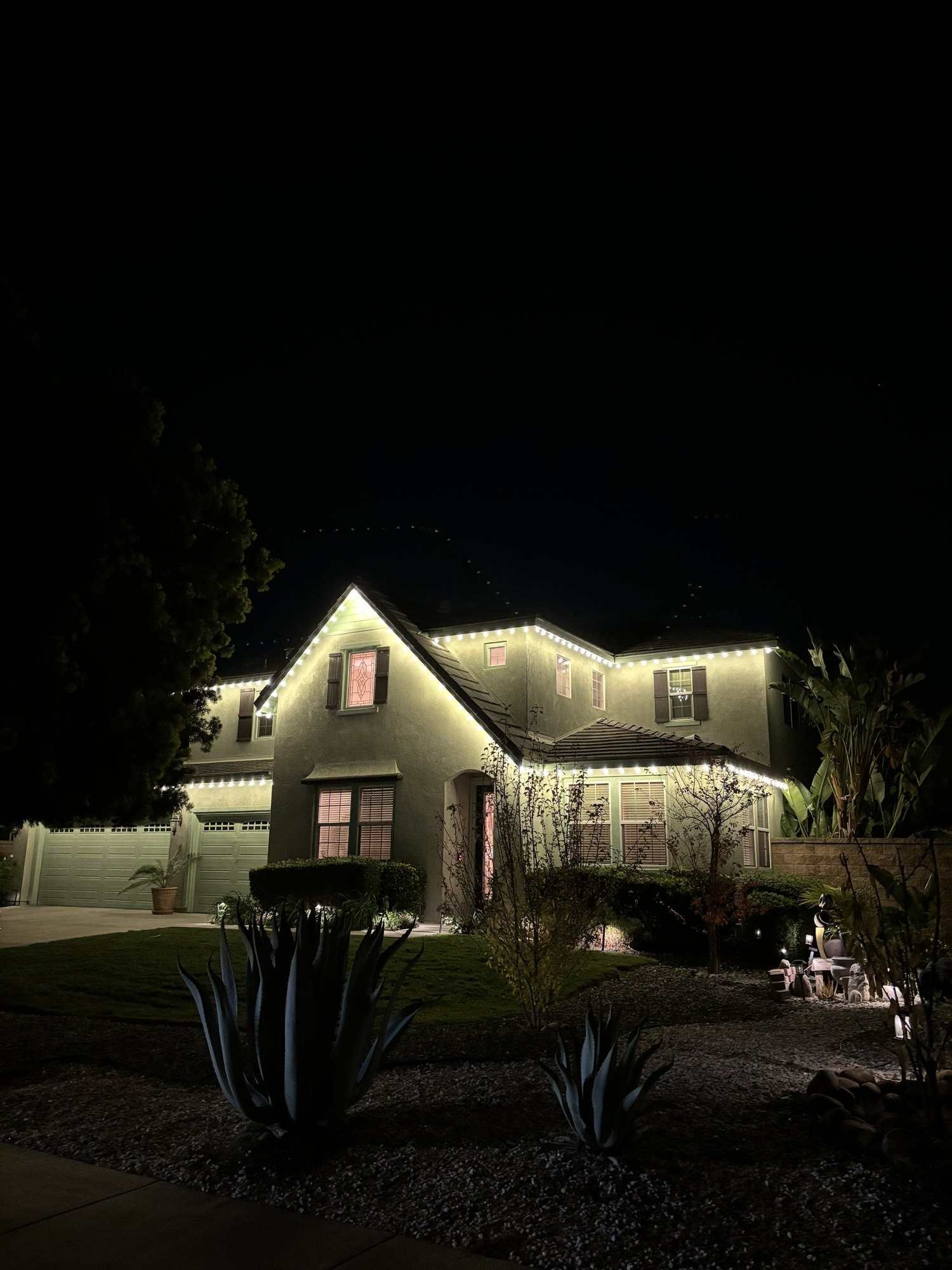 Gable roofline of a two-story home outlined in warm white Christmas lights